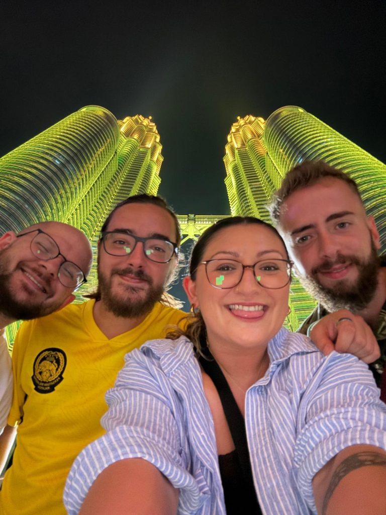 Four Travelogue Guesthouse guests in a selfie with the Petronas Twin Towers lit behind them