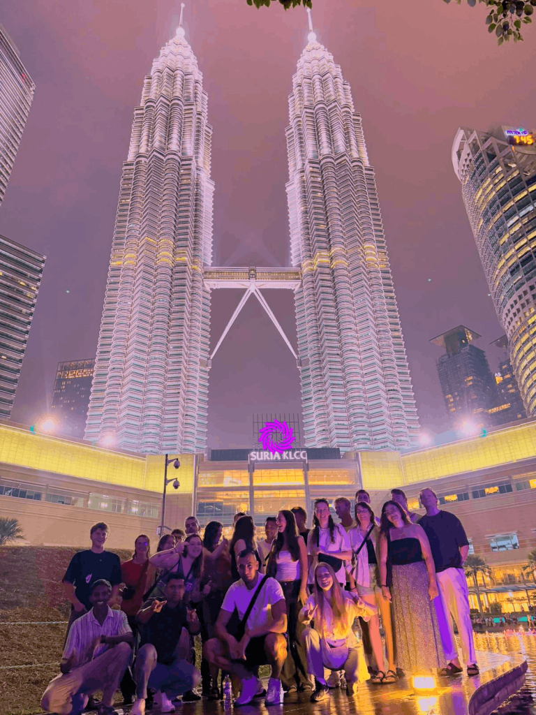 A large Travelogue Guesthouse group on the steps below the Petronas Twin Towers at night