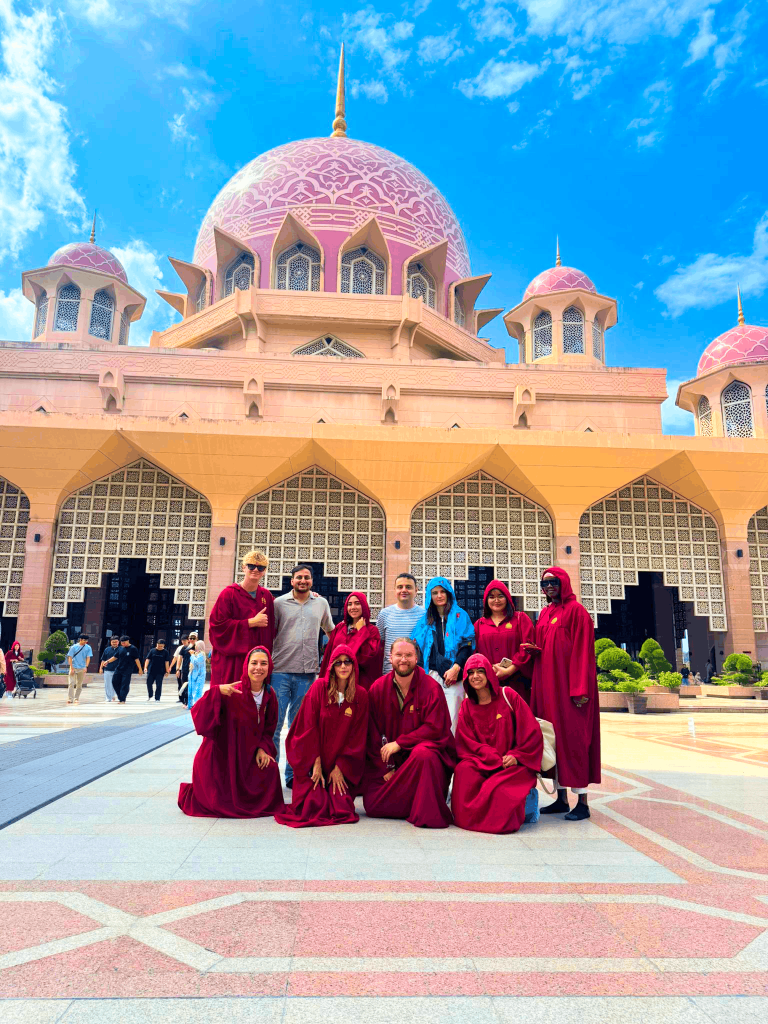 Travelogue Guesthouse guests in visitor robes outside a pink domed mosque