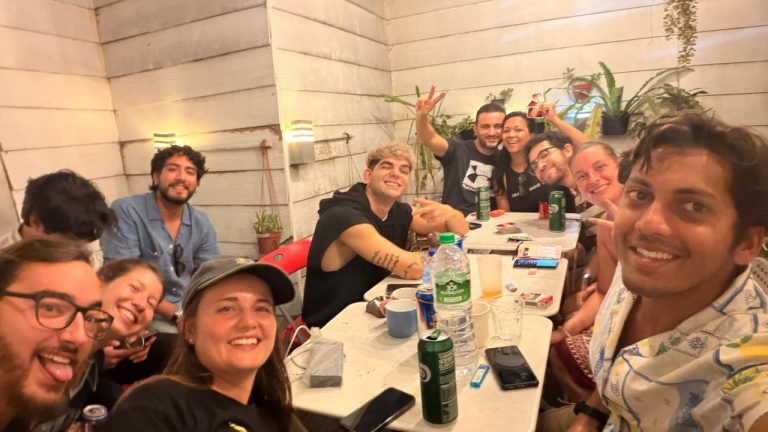 Travelogue Guesthouse guests round a table with drinks, everybody talking at once