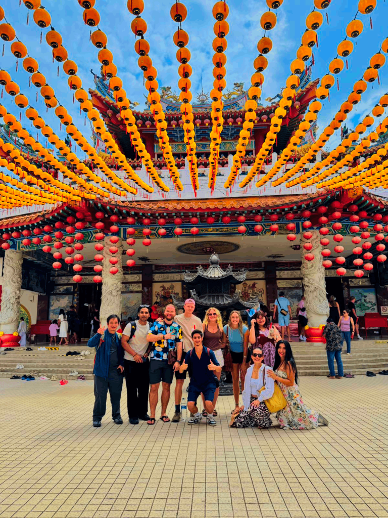 A Travelogue Guesthouse group under a ceiling of hanging orange lanterns at a temple