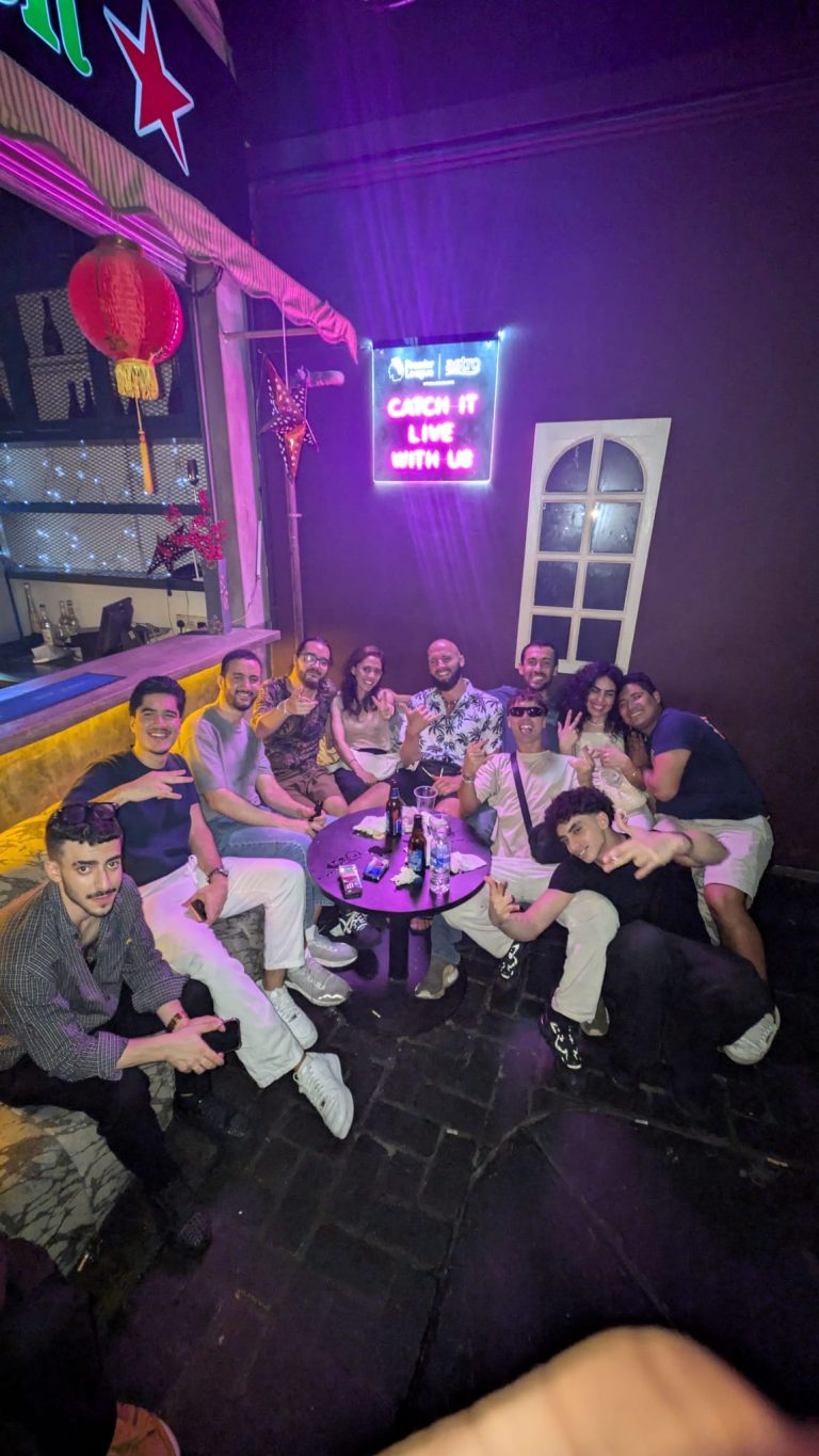 Travelogue Guesthouse guests round a table under purple bar lighting
