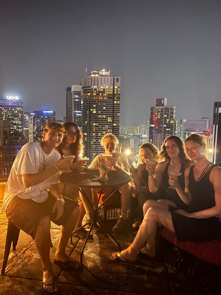 Guests at a rooftop table at night with the lit Kuala Lumpur skyline behind