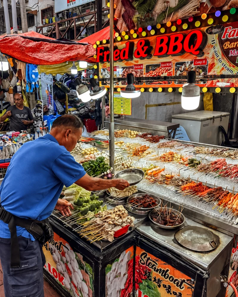 A cook turning skewers over the grill at a Jalan Alor stall, Kuala Lumpur