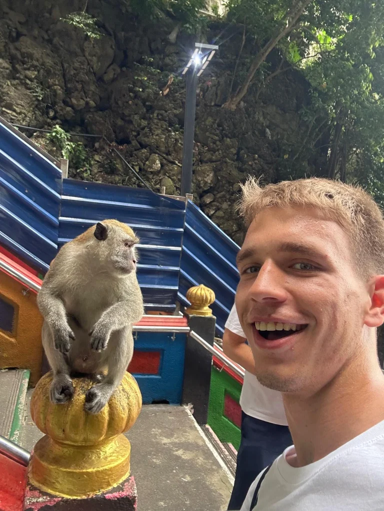 A Travelogue Guesthouse guest beside a macaque sitting on the rail of the Batu Caves steps