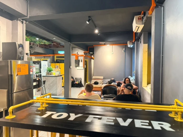 A long black bar table with a yellow rail, looking across the common area to guests on the sofas at Travelogue Guesthouse