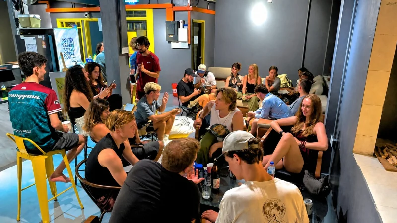 Twenty or so guests sitting together on sofas, stools and the floor in the common area at Travelogue Guesthouse, Bukit Bintang