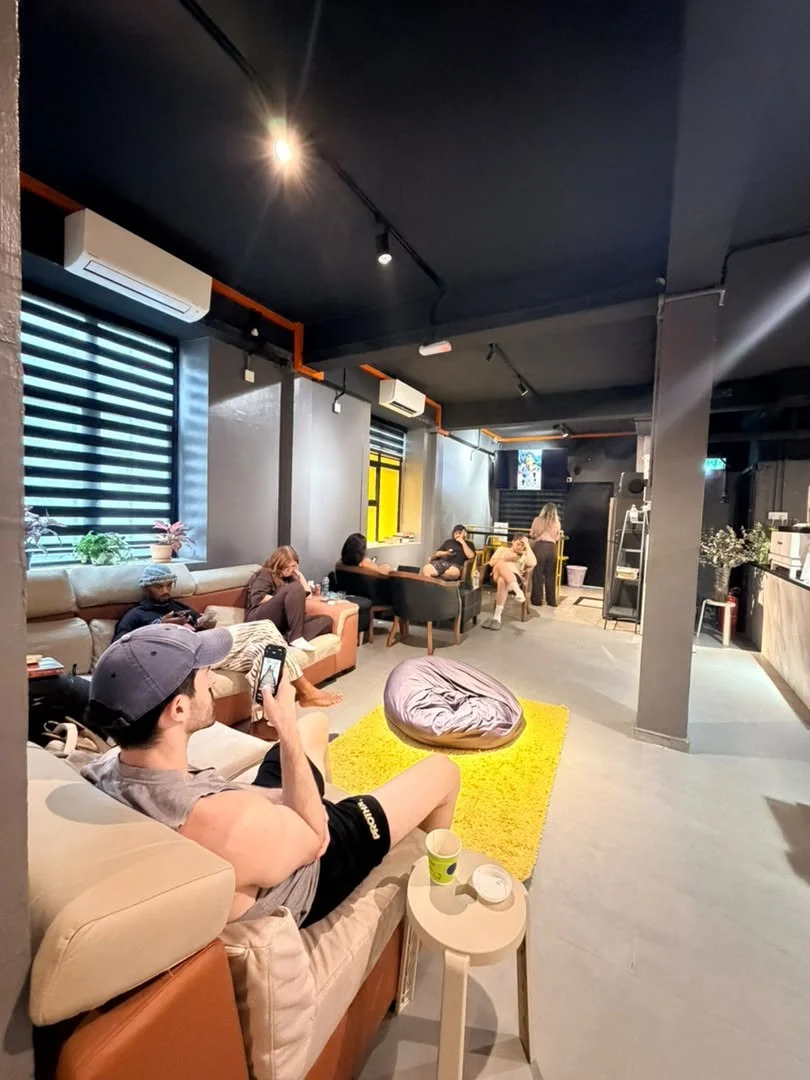 Guests on the sofas in the common area at Travelogue Guesthouse, one on a phone, with a yellow rug and a beanbag