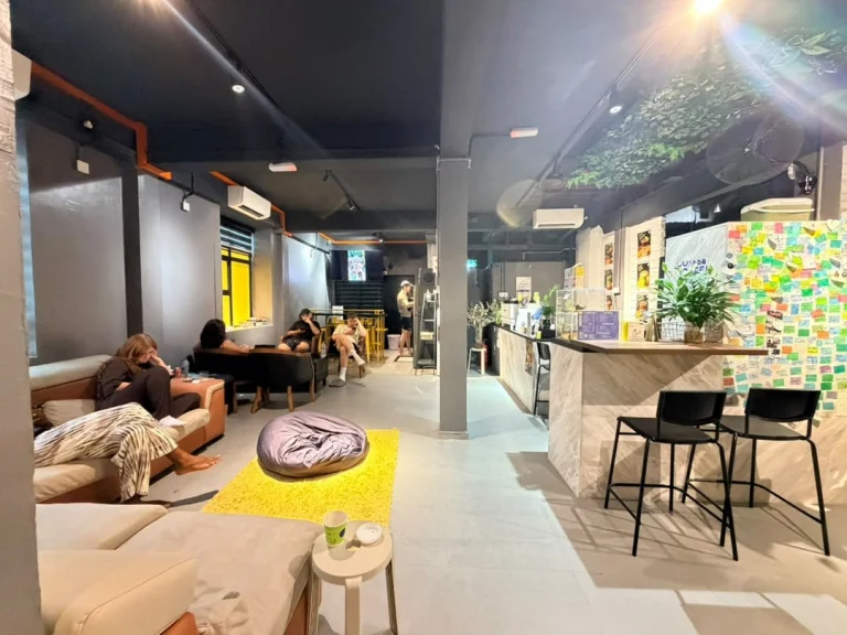 The common area at Travelogue Guesthouse: sofas, a yellow rug and a beanbag, with the counter and bar stools to the right