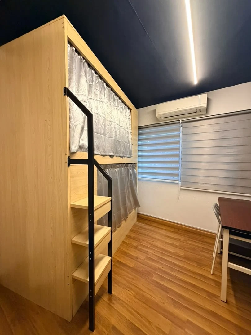A wooden pod bunk with grey privacy curtains and a built-in ladder beside a window, in a dormitory at Travelogue Guesthouse