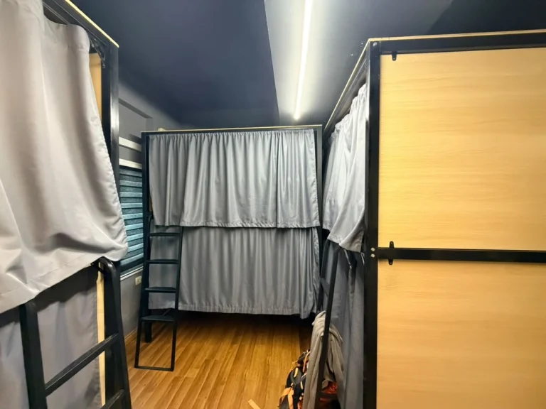Three metal-framed bunks with grey curtains around a dormitory at Travelogue Guesthouse, Kuala Lumpur