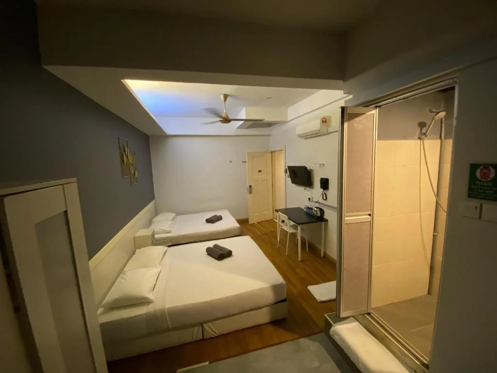 The family room at Travelogue Guesthouse: a double and a single bed, a wall-mounted television and the glass shower cubicle of its own bathroom
