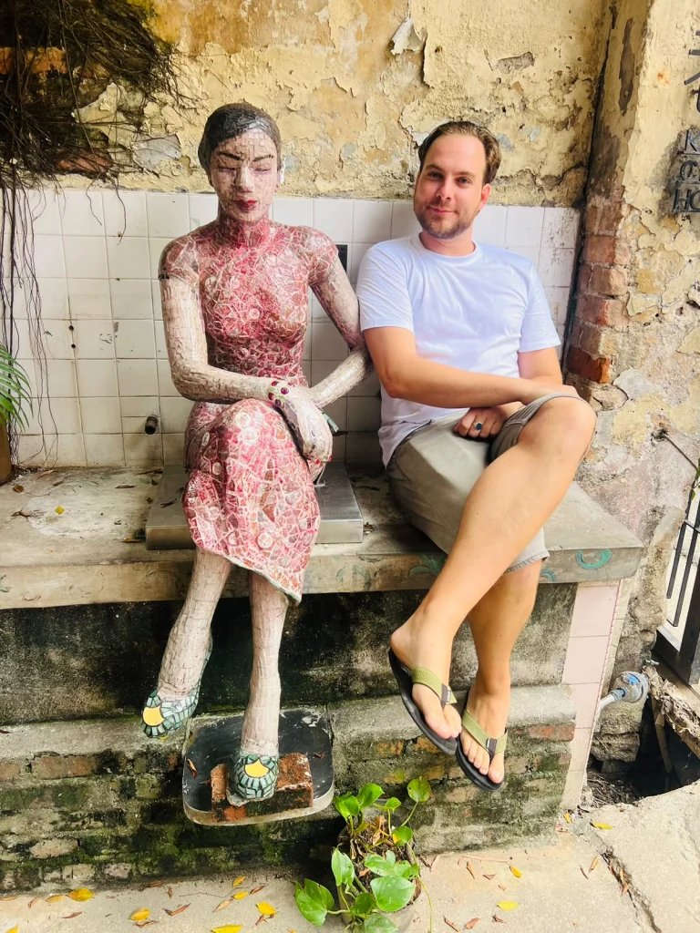 A Travelogue Guesthouse guest beside a seated sculpture in Graffiti Alley, Bukit Bintang