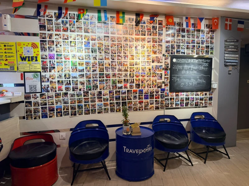 The wall of guest photographs at Travelogue Guesthouse under a line of national flags, with the activities chalkboard beside it