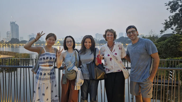 Travelogue Guesthouse guests at a railing by the water with the city behind