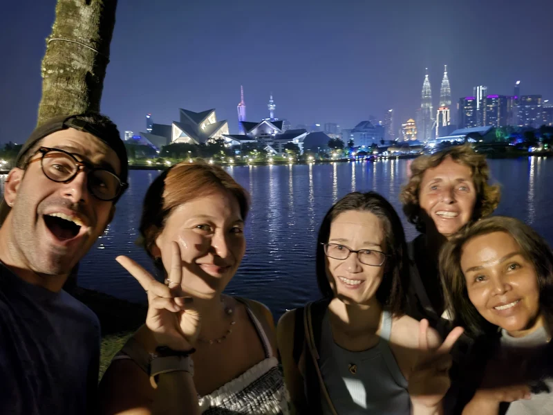 Travelogue Guesthouse guests with the lit Kuala Lumpur skyline across the water behind them