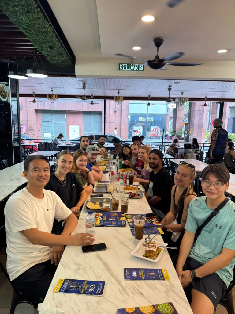 Travelogue Guesthouse guests along one long table over dinner in Kuala Lumpur