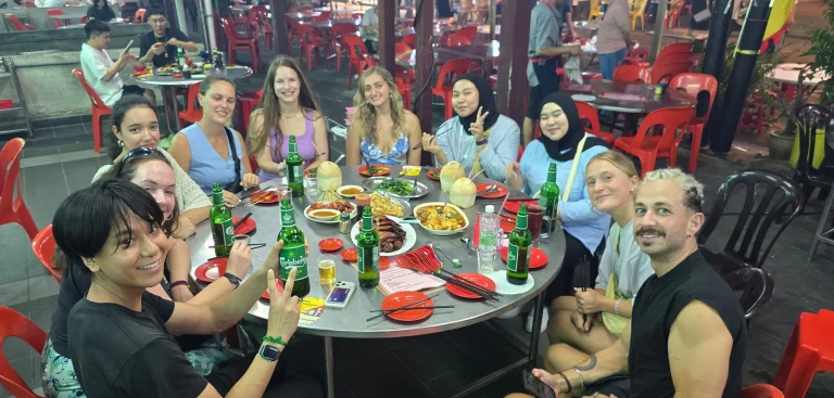 Travelogue Guesthouse guests around an outdoor table of food and drinks at night