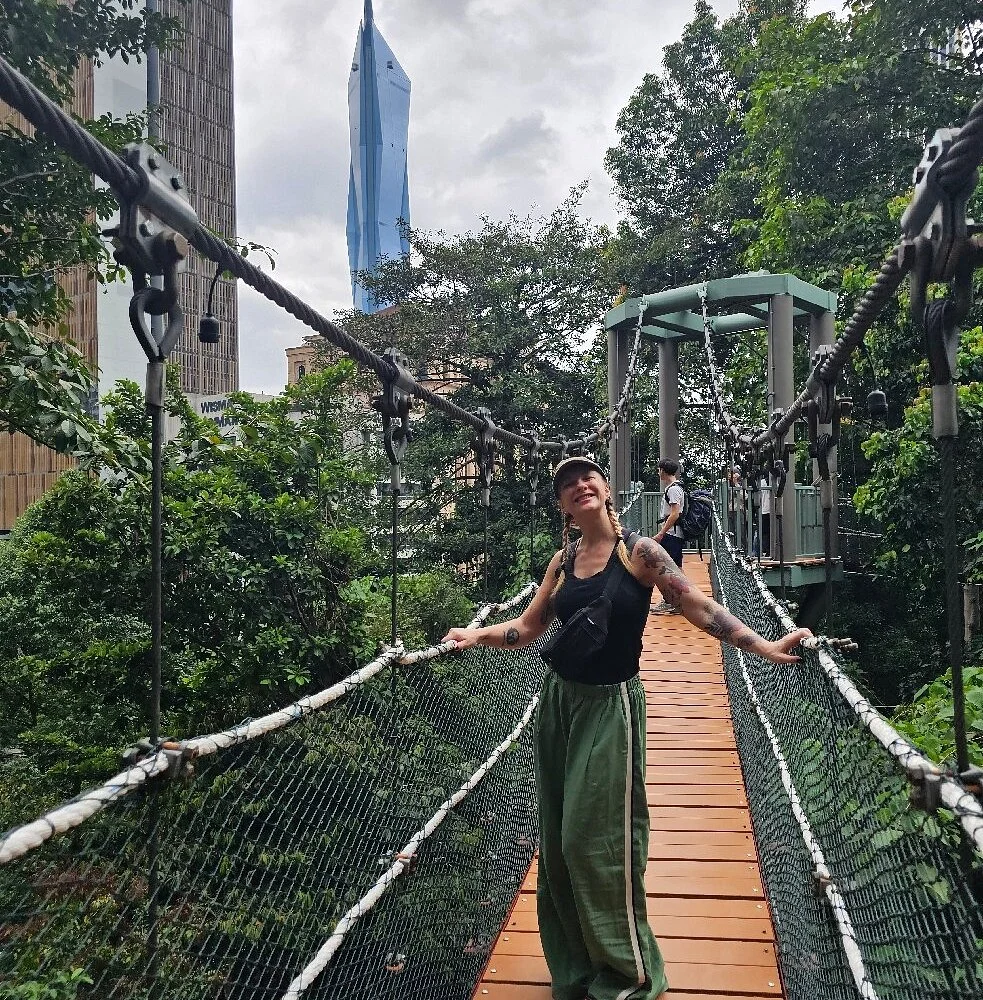 A walker on the suspended canopy walk at KL Forest Eco Park, with the city towers behind