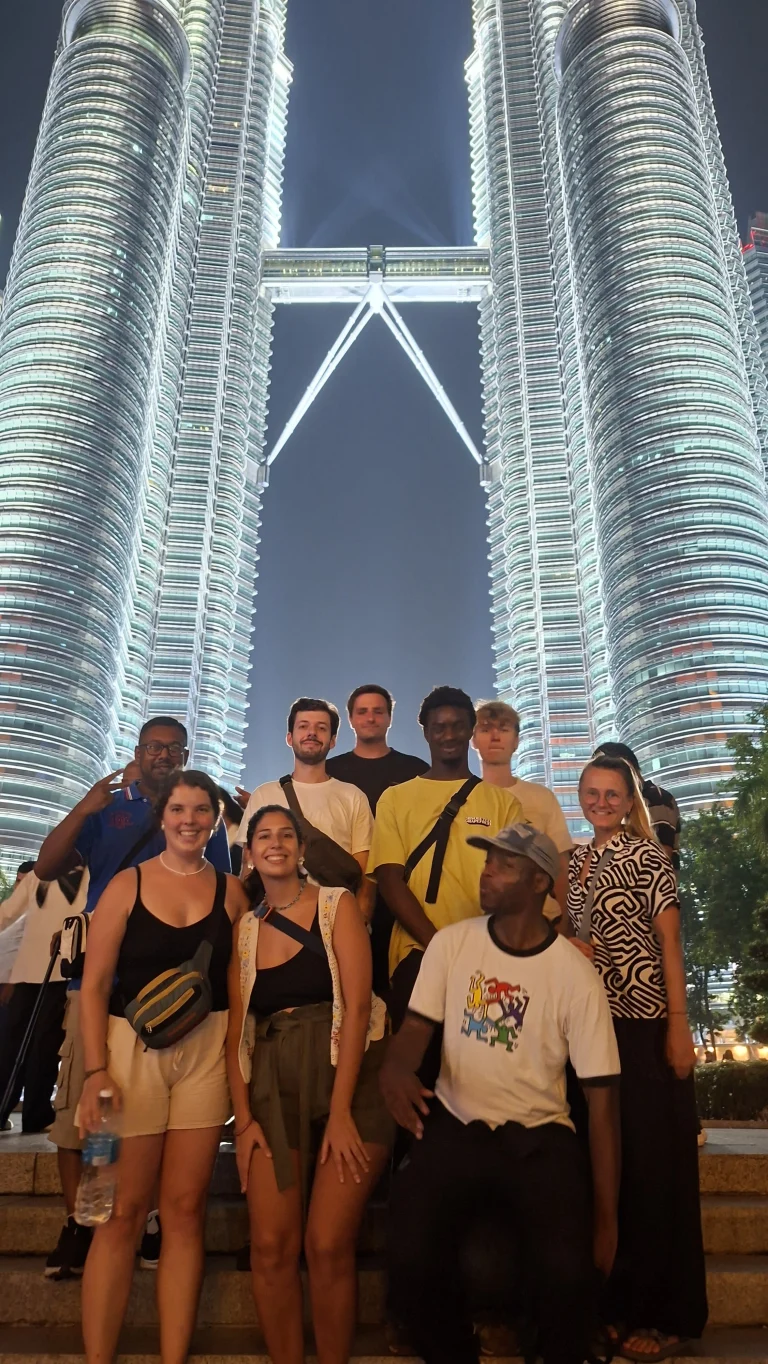 A Travelogue Guesthouse group standing below the lit Petronas Twin Towers