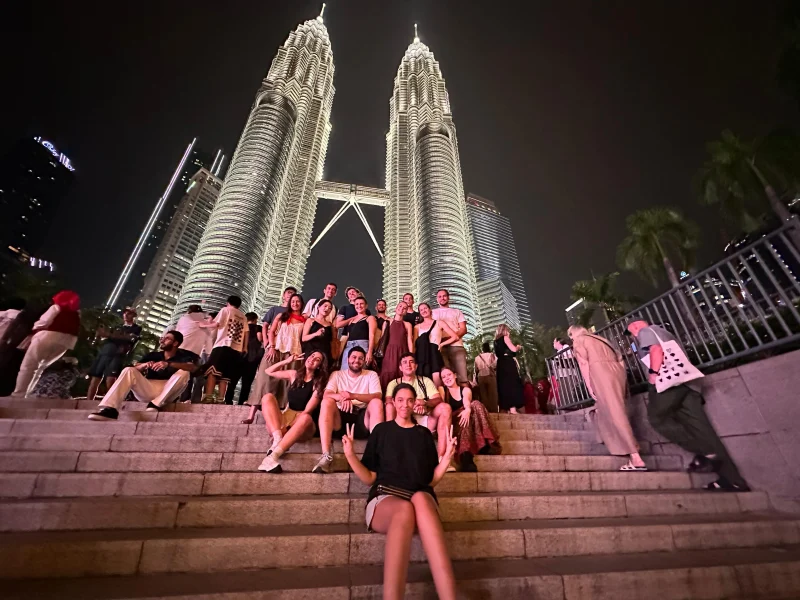 Travelogue Guesthouse guests on the steps below the Petronas Twin Towers at night, Kuala Lumpur
