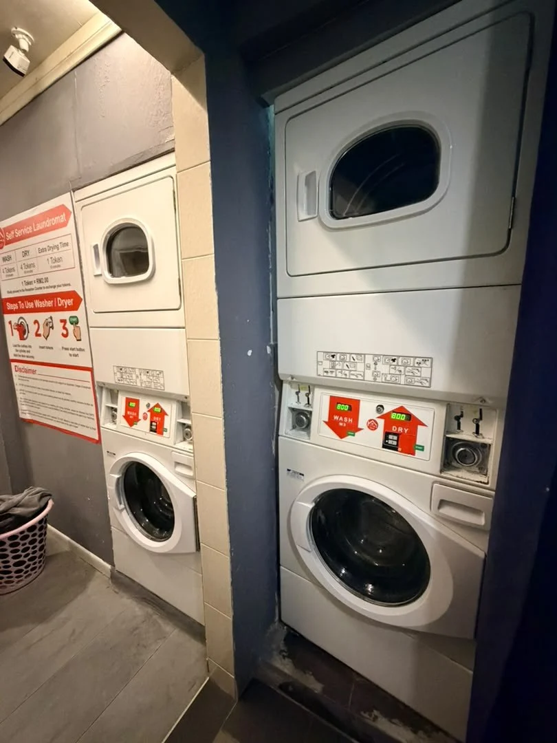 Another set of stacked washers and dryers beside the self-service laundry instructions at Travelogue Guesthouse