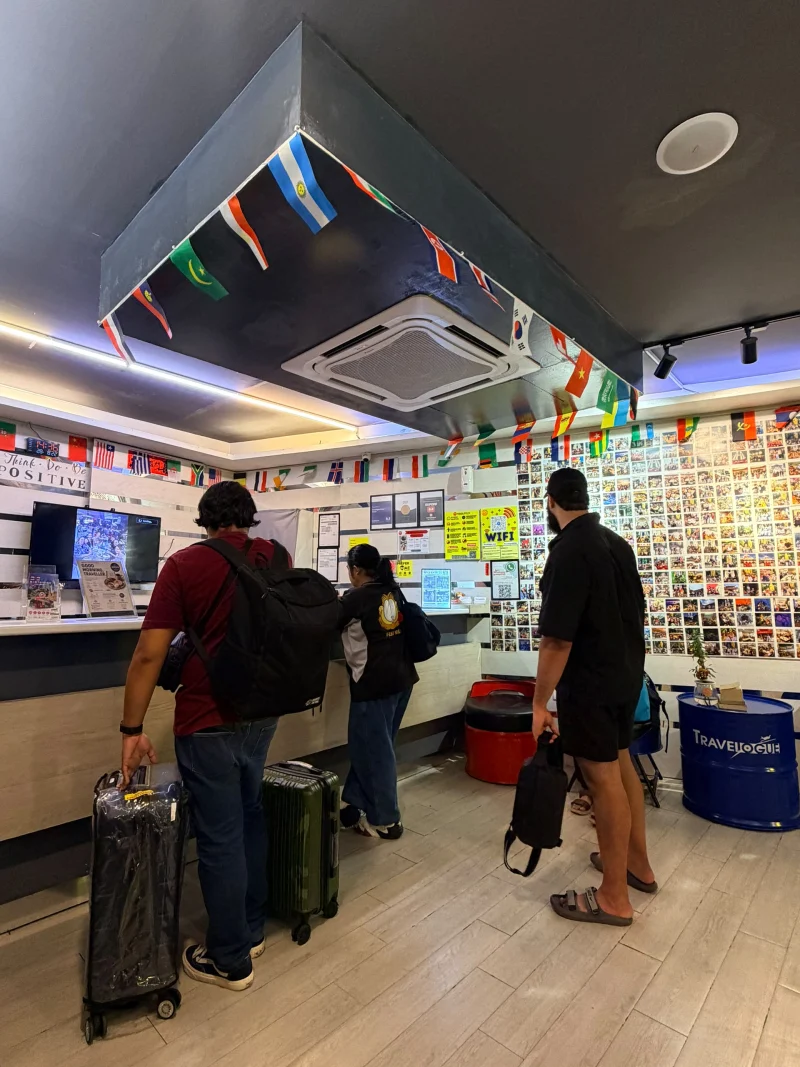 Backpackers checking in at Travelogue Guesthouse reception under a ceiling of world flags, Bukit Bintang, Kuala Lumpur