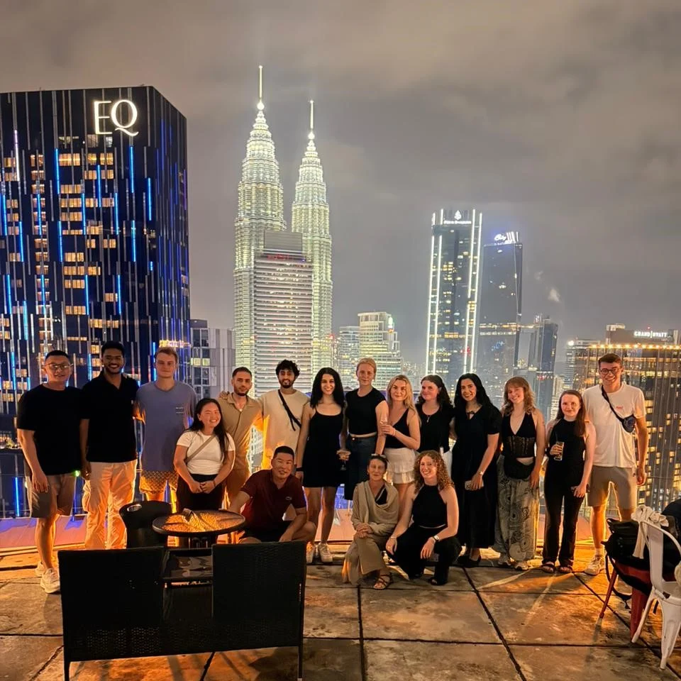 Travelogue Guesthouse guests on the rooftop at night with the Petronas Twin Towers lit up behind them
