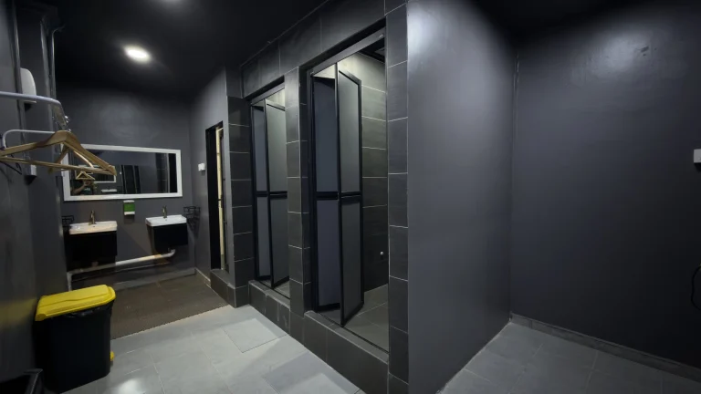 The shared bathroom at Travelogue Guesthouse, with a basin under a mirror and a row of cubicle doors