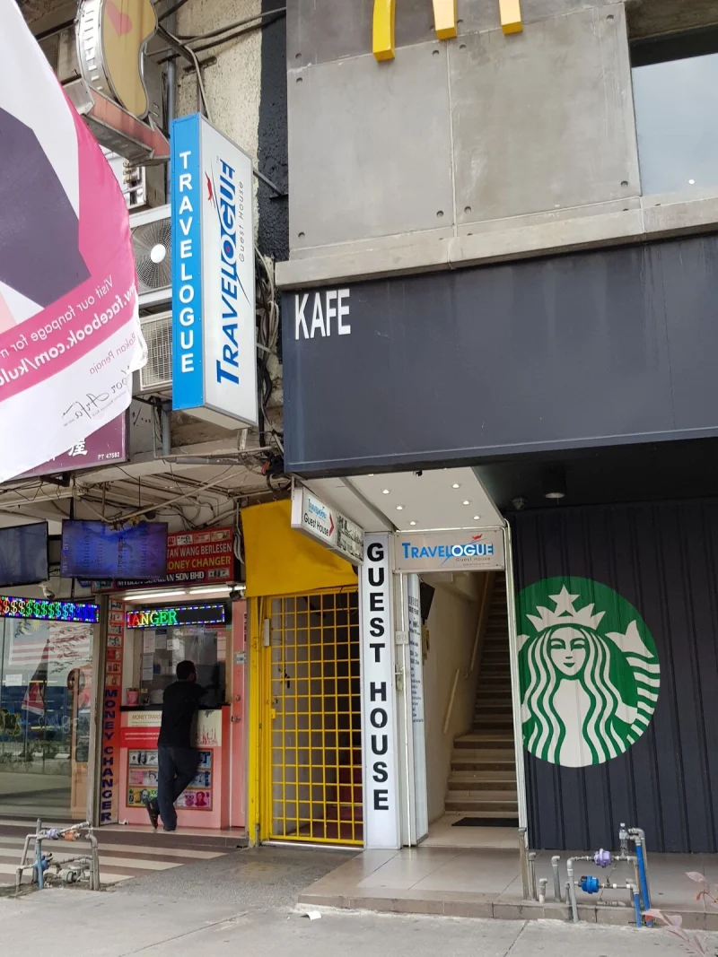 The Travelogue Guesthouse street entrance on Jalan Bukit Bintang: a yellow doorway signed Guest House, immediately beside a Starbucks