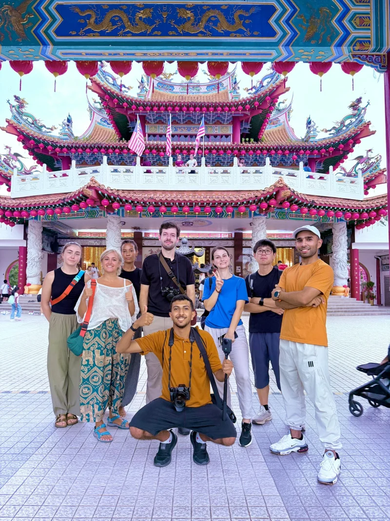A Travelogue Guesthouse volunteer crouching with his camera in front of a group of guests on the steps of Thean Hou Temple, Kuala Lumpur