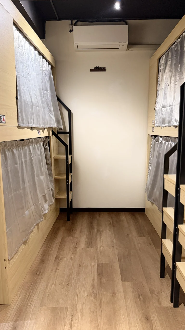 Pod bunks with pale curtains either side of the aisle in the female dormitory at Travelogue Guesthouse
