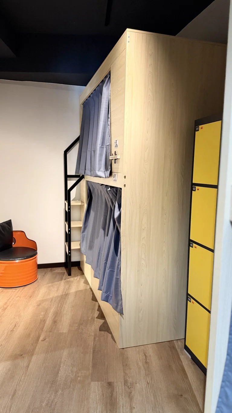 A pod bunk, a yellow locker door and an orange stool in the female dormitory at Travelogue Guesthouse